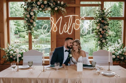 Napis świetlny &bdquo;Miłość&rdquo; nad stołem Pary Młodej &ndash; elegancka dekoracja na wesele